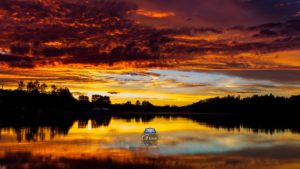 Photograph of a cloudy sunset reflected over water with Grace Bible Church logo
